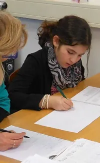 Een docent helpt een leerling die aan tafel een werkblad invult